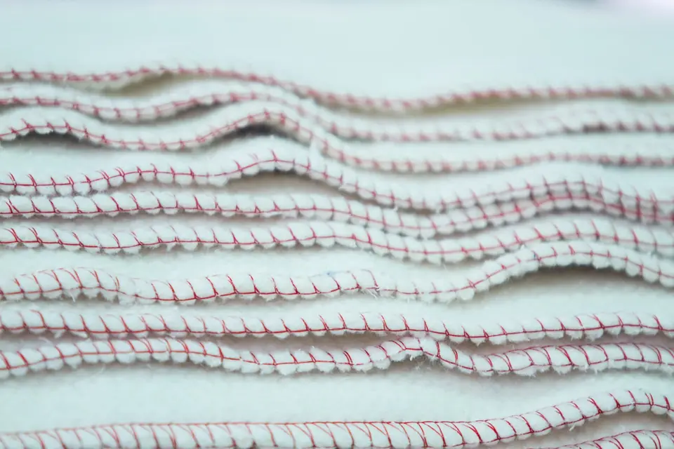 Close-up of stacked white textile cloths finished with red overlock stitching along their edges.